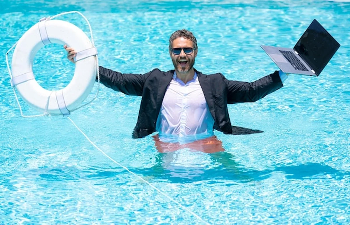 Biznesmen w garniturze trzymający laptop i bojkę ratunkową na plaży