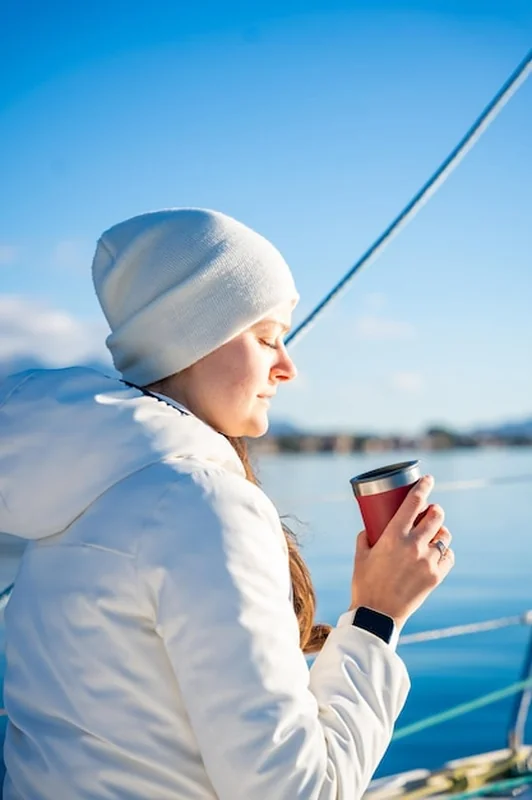 Ręce kobiety trzymające kubek termiczny na jachcie podczas żeglugi rano w zimie