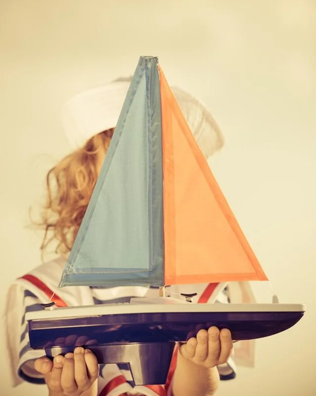 Szczęśliwe dziecko bawiące się zabawkową żaglówką na tle błękitnego nieba